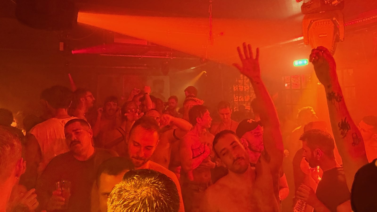 Men dancing in a crowded room covered in red lights.