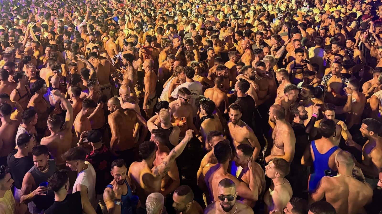 A huge crowd of topless men dancing at night.