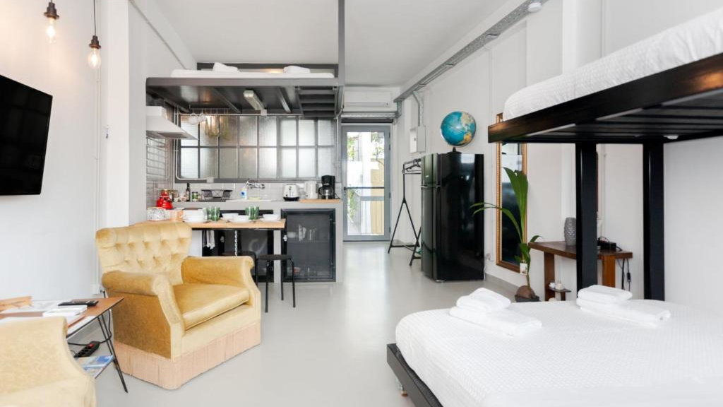 A white and black industrial style room with lounge chairs, bunk beds and a small kitchenette.