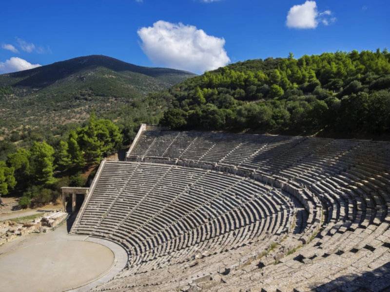 Looking down into an ancient amphitheater surrounded by hills and forest.