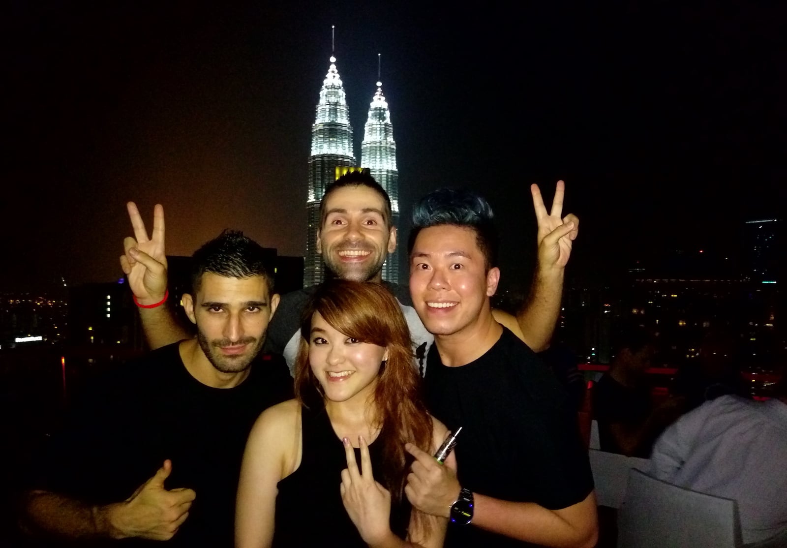 Stefan and Seby posing with two friends at night at a rooftop bar with two towers lit up behind them.