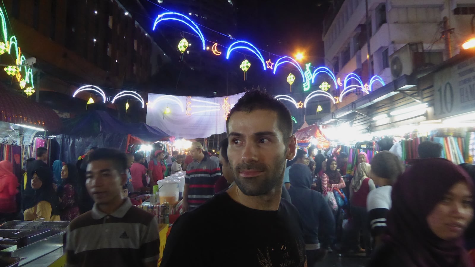 Seby looking away from camera in a night market with lots of people around.