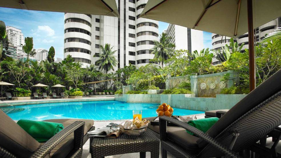 The view from lounge chairs looking at a tropical pool with high-rise towers in the background.