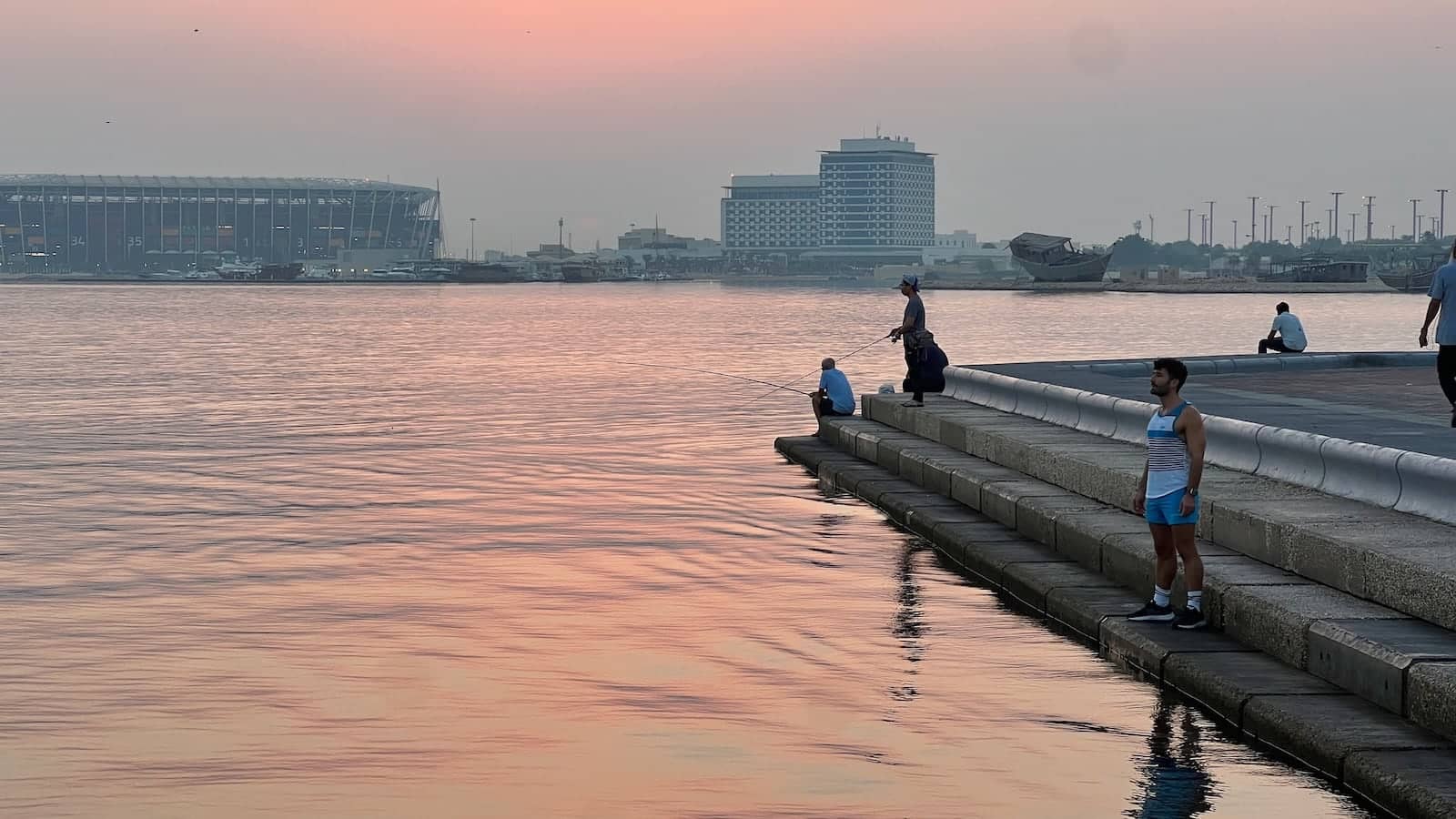 Stefan standing on steps next to water at sunset with some fishermen behind him.