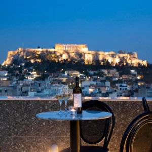 A table with wine and glasses on a balcony at night overlooking the Acropolis in Athens.