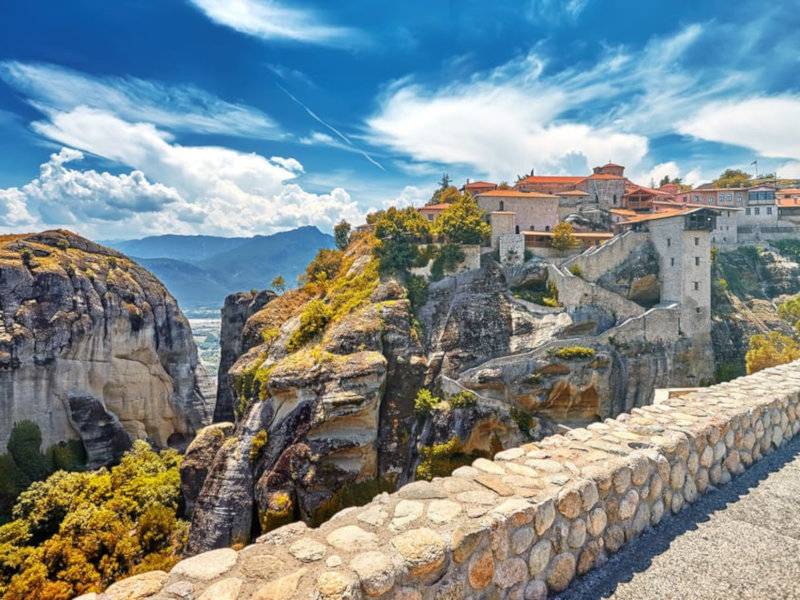 A rocky wall looking out towards buildings perched on epic cliffs.