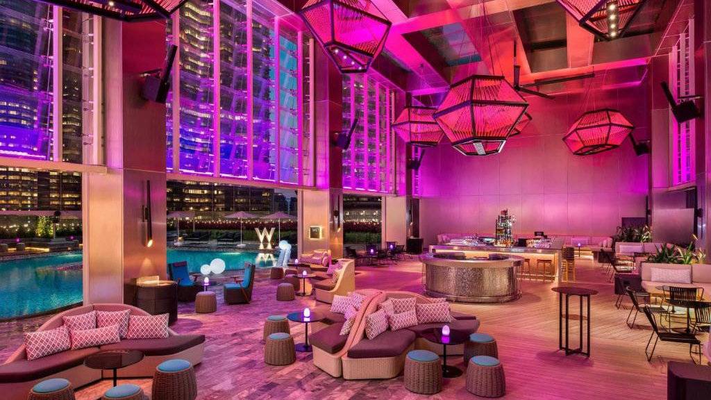 A glamorous poolside bar lit up in pinks and purples at night.