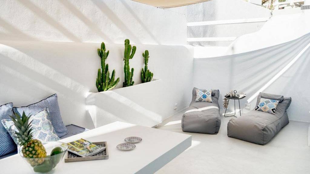 A sun-drenched white courtyard with lounges, a table and chairs and cacti.