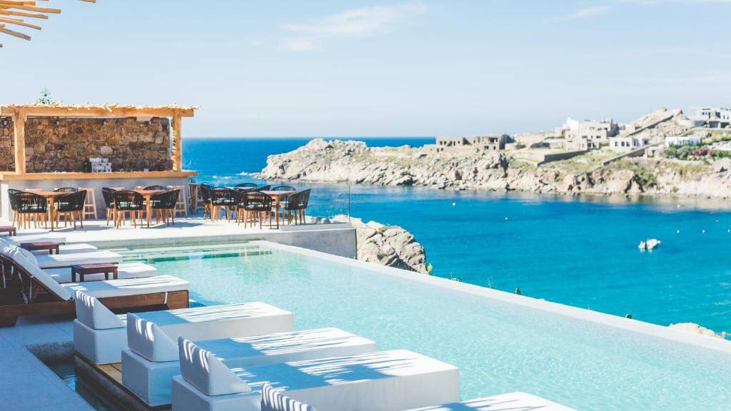 An epic infinity pool with sunbeds and restaurant area, perched directly next to a rocky bay.