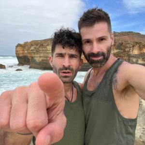 Stefan and Seby wearing green singlets and Stefan pointing directly into the camera with ocean and rocks behind them.