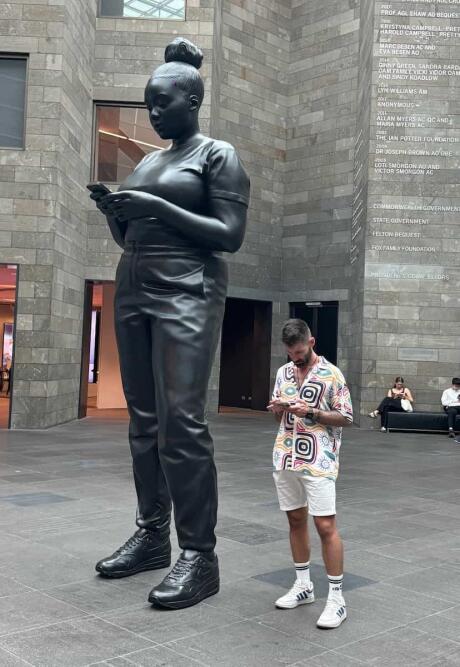 Sebastien at the Melbourne NGW National Gallery Victora next to the statue holding a phone.